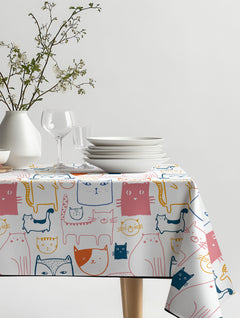 Mantel de hule Cats con gatos dibujados en rosado, naranjo, amarillo y azul marino, sobre una mesa de comedor