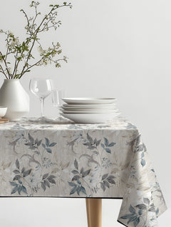 Mantel de hule Eliot con ramas de hojas en gris, azul grisáceo y beige, sobre una mesa de comedor