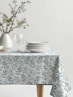 Mantel de hule Ramitas con hojitas de acuarela en verde grisáceo y blanco, sobre una mesa de comedor
