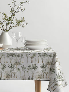 Mantel de hule Rosa Tropical con palmeras y hojas de plátano en verde salvia, beige y blanco, sobre una mesa de comedor