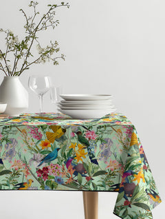 Mantel de hule Tropical Paradise II con aves y flores en azul, amarillo, rosado y verde menta, sobre una mesa de comedor
