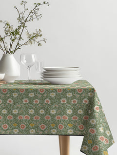 Mantel de hule Windsor con margaritas coral, crema y mostaza entre follaje verde salvia, sobre una mesa de comedor